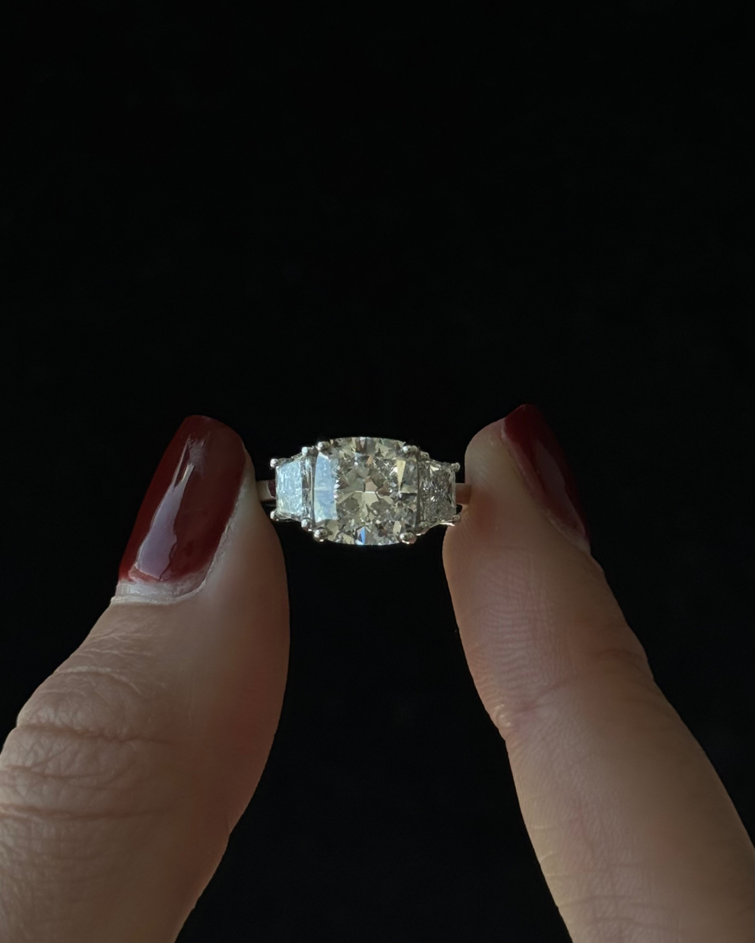 Diamond ring held between two fingers against a black background