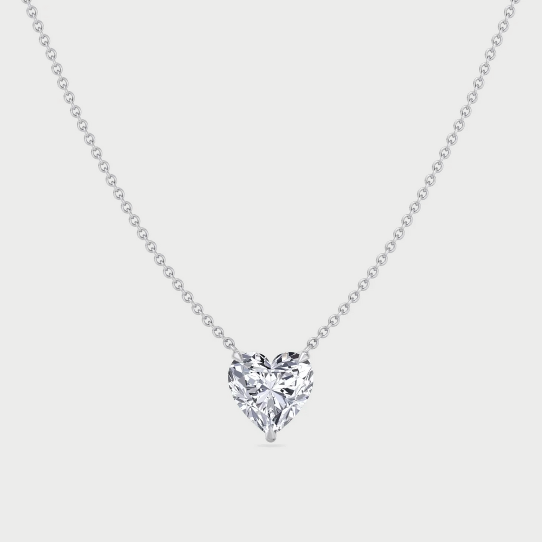 Heart-shaped diamond pendant on a chain against a light gray background