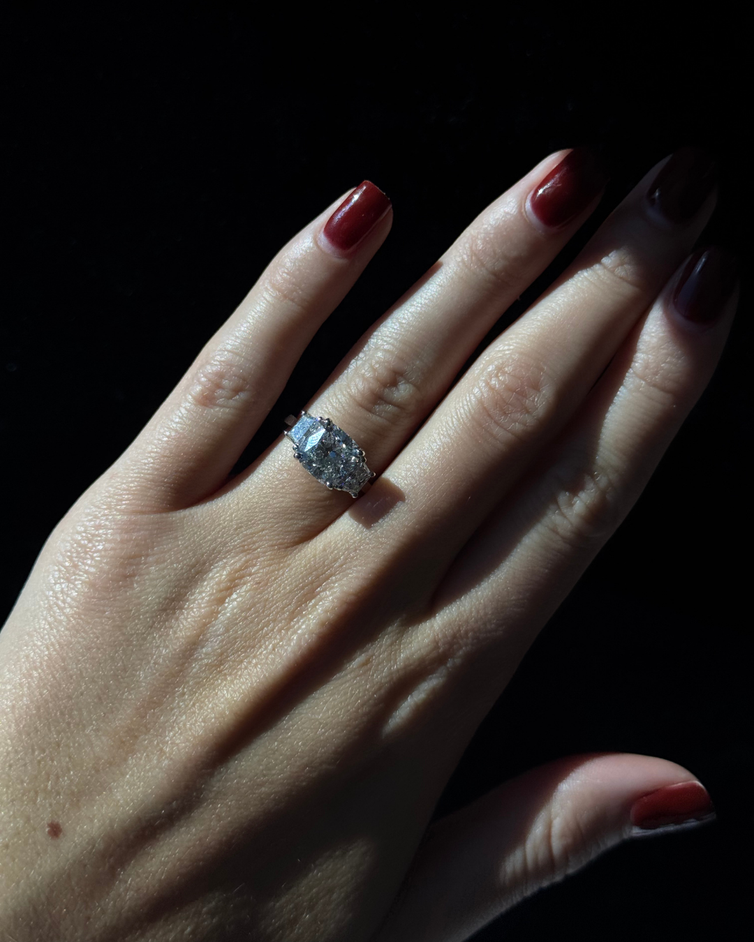 Hand wearing a diamond ring with a dark background
