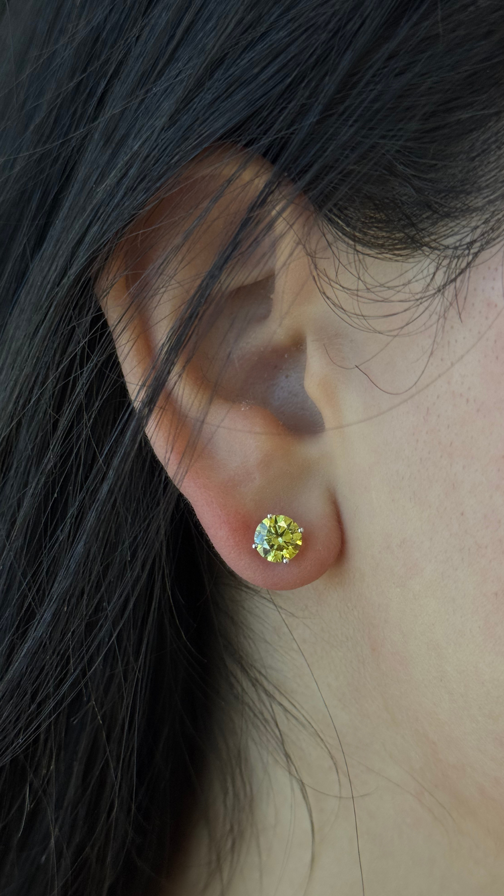 Close-up of an ear wearing a round yellow gemstone earring with dark hair.