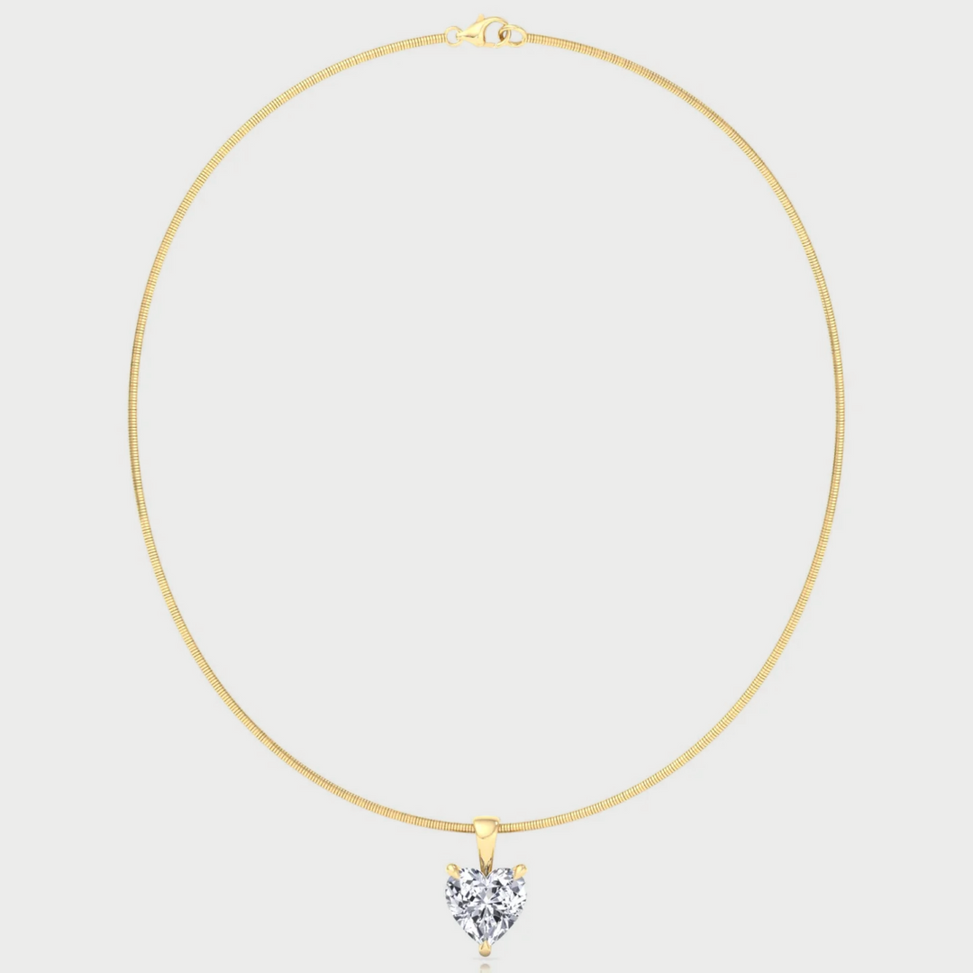 Gold necklace with a heart-shaped diamond pendant on a light gray background