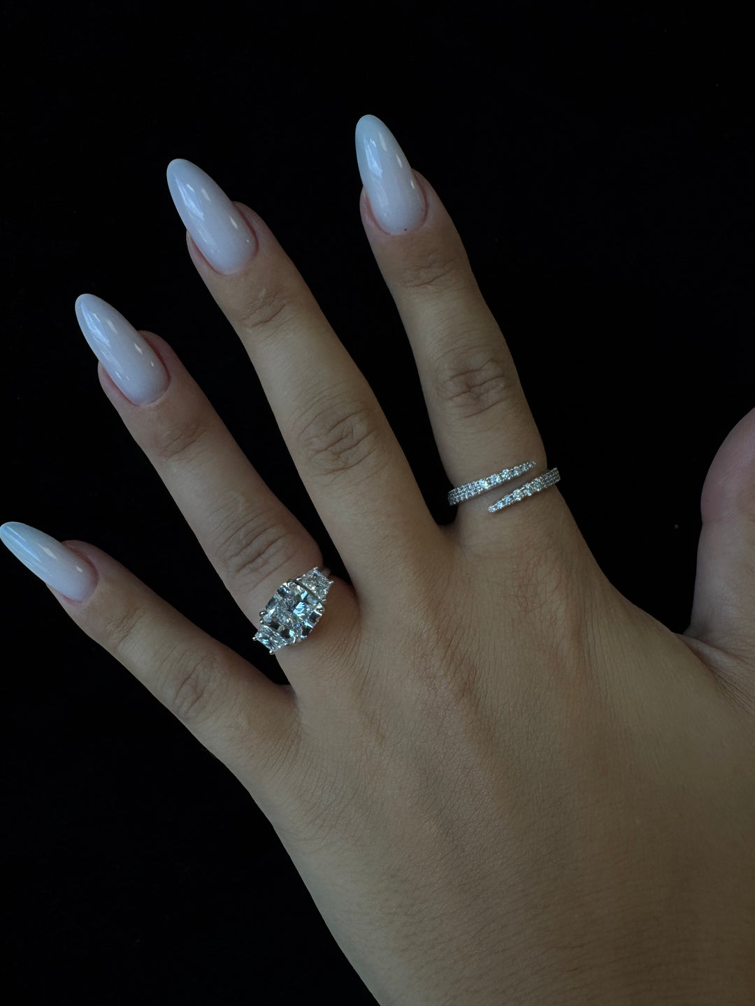 Hand wearing two diamond rings on a black background