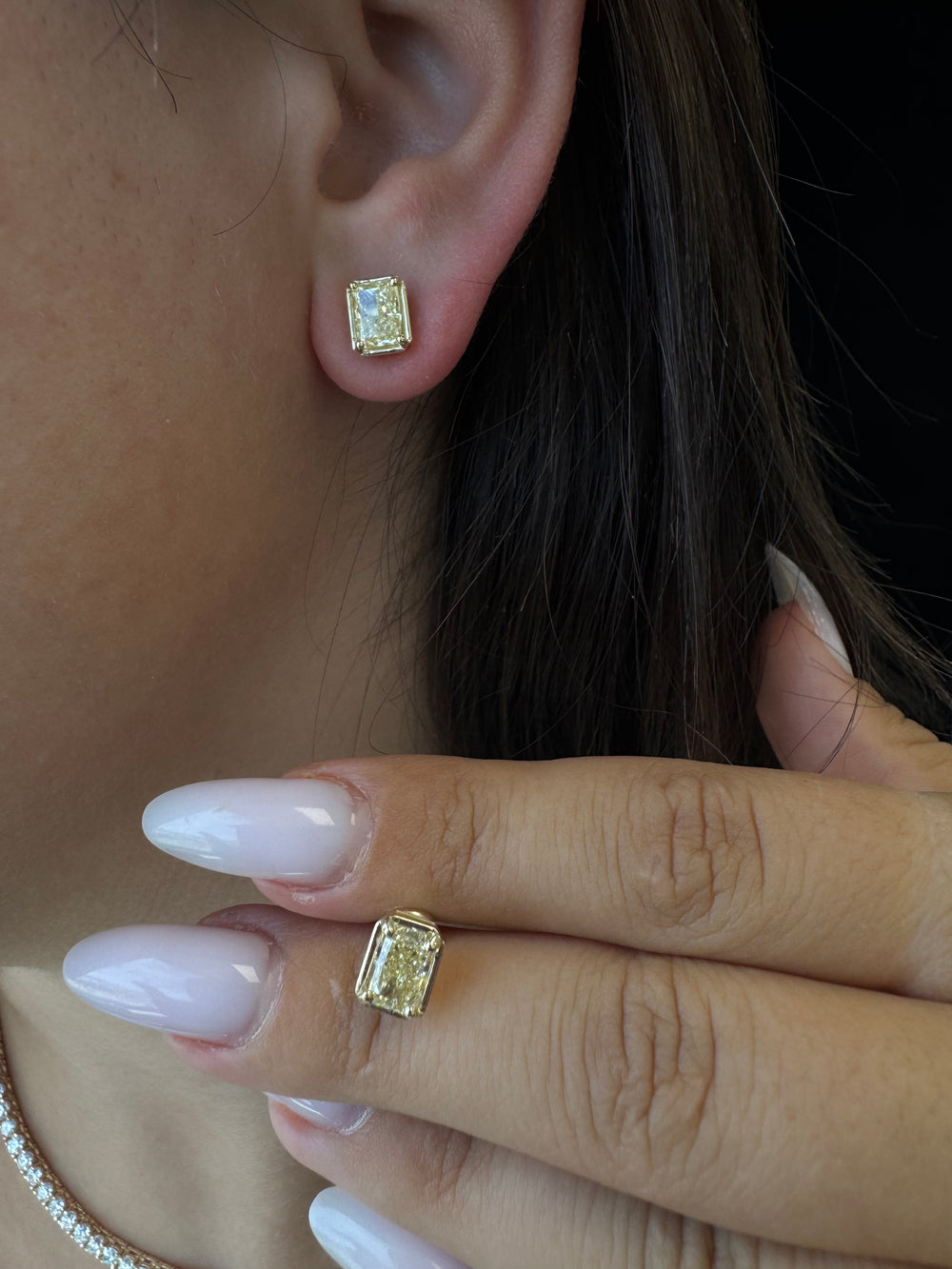 Close-up of a hand with a ring and ear with an earring, both featuring yellow gemstones.