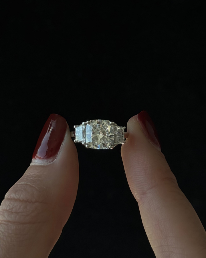 Diamond ring held between two fingers against a black background