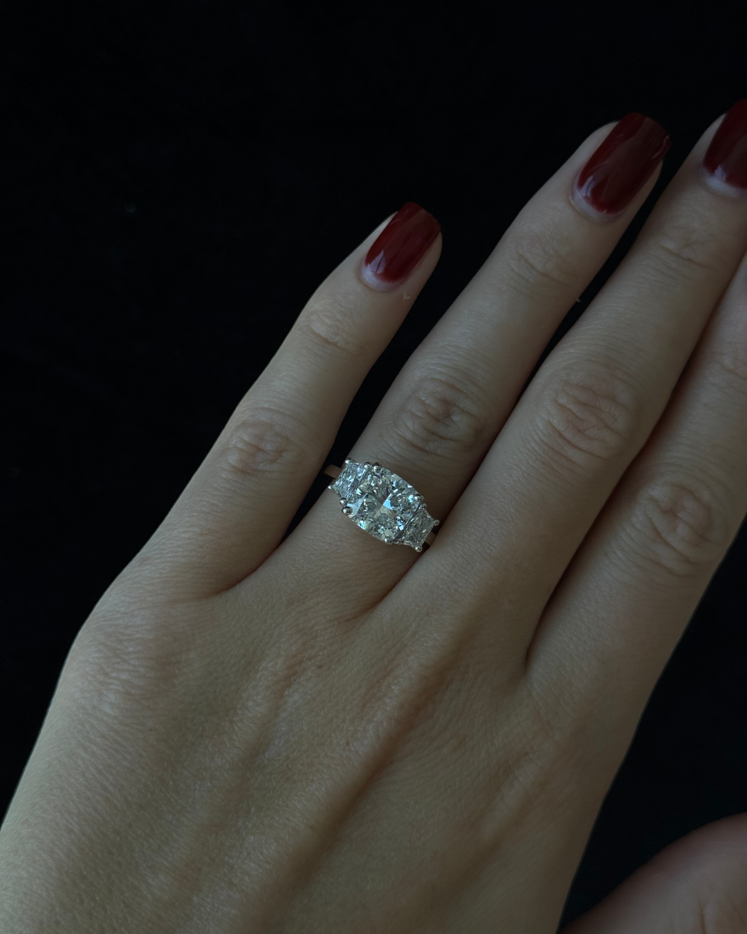 Hand wearing a diamond ring with a dark background