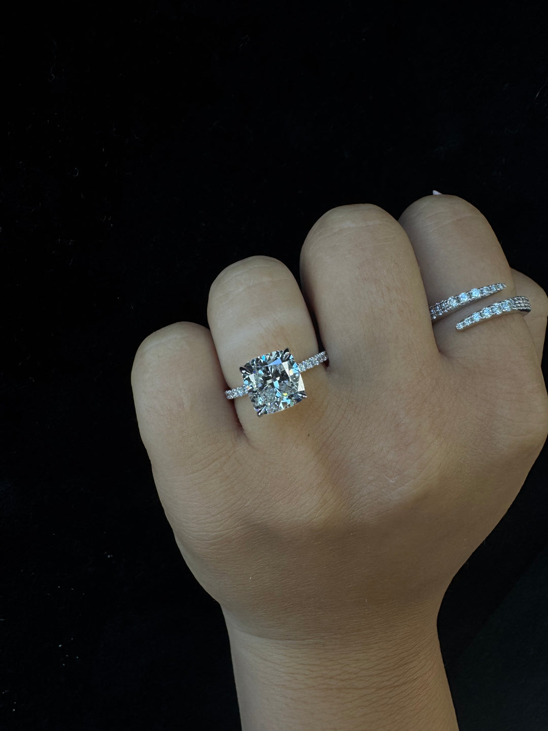 Hand wearing two diamond rings on a black background