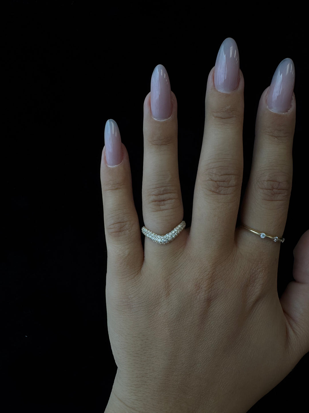 Hand wearing two rings on a black background